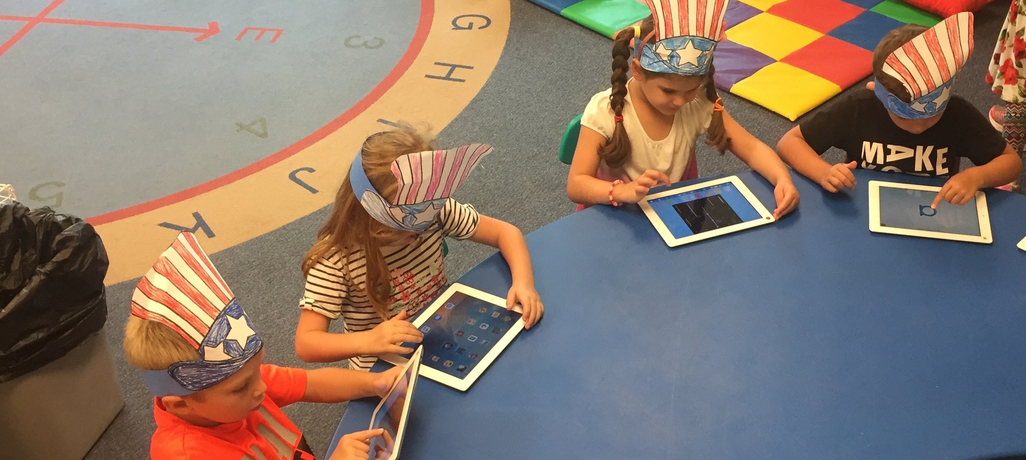Students working on iPads with hats on that look like flags