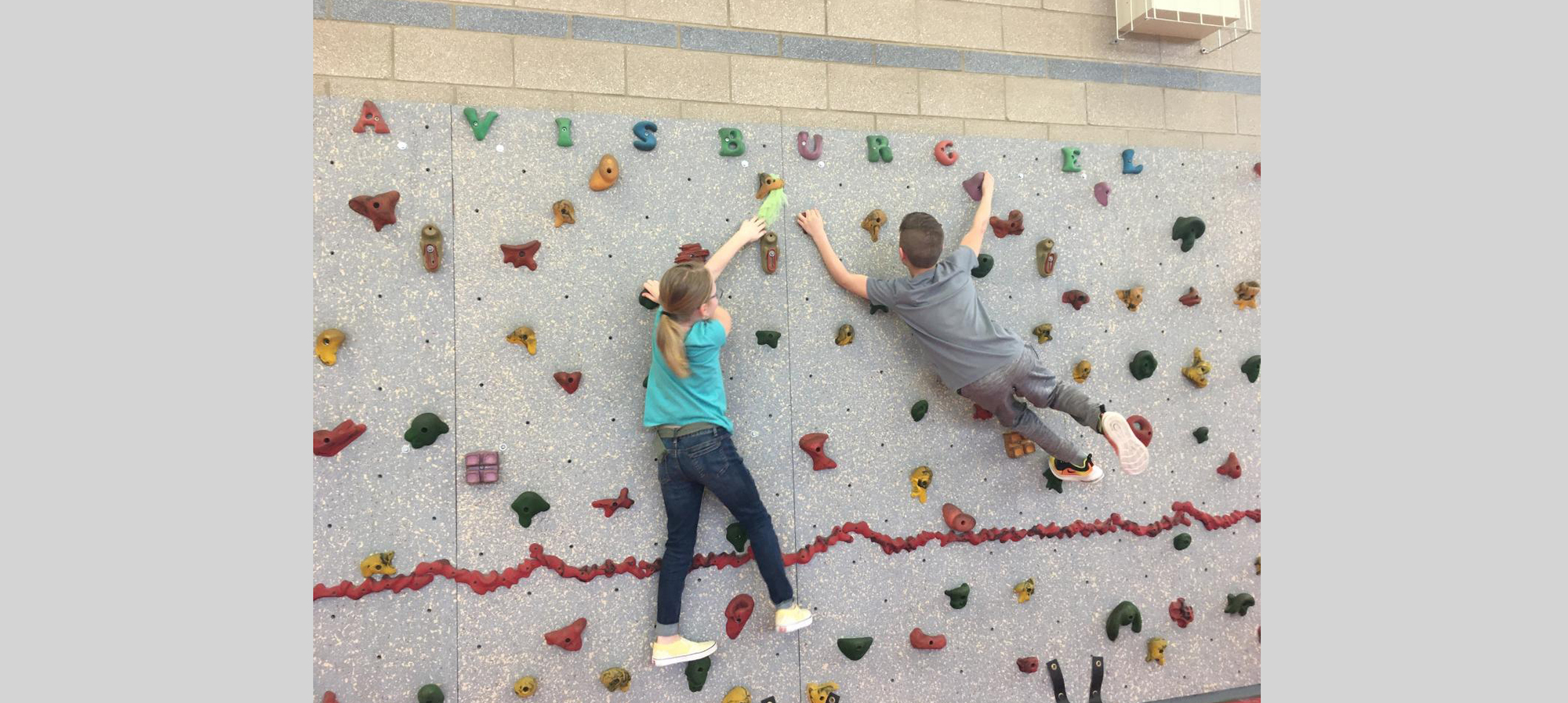 Two students climbing on the climbing wall in the gym.